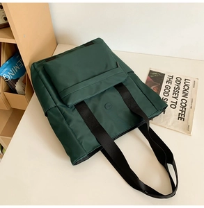 Close-up of a dark green nylon tote bag featuring a front pocket and wide black straps