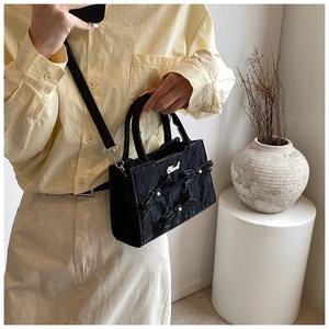 Detailaufnahme der schwarzen Stepptasche mit Schleifen, Perlen und silbernem Metalllogo