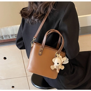 Detail of dark brown bucket bag with double handles and a cute bear leather charm