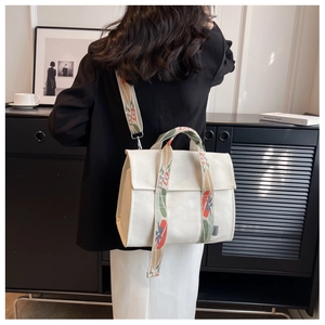 Detail of white canvas tote bag featuring colorful floral embroidered wide shoulder strap