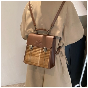 Detail view of brown leather and plaid backpack on a model wearing a beige trench coat