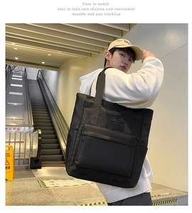 Detail of a large black nylon tote bag showing spacious design and side pocket in outdoor setting