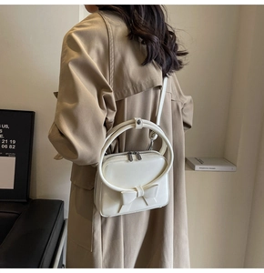Detail of white square crossbody bag with bow accent and round metal handle