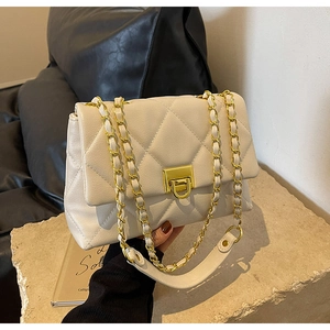 Detailed close-up of cream quilted crossbody bag with gold chain strap on stone pedestal
