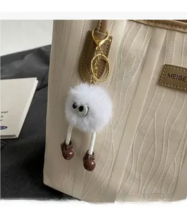 Close-up of white plush monster charm with long legs on a striped tote bag strap