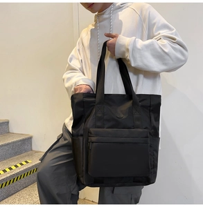 Detailed view of black nylon tote bag with large zipper front pocket and shoulder straps