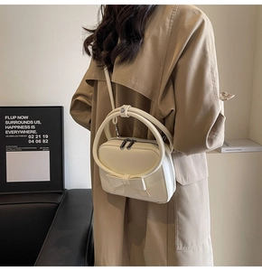 Crossbody view of a cream leather square handbag with bow and round handle on a model