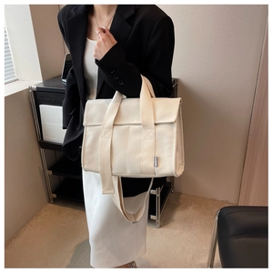 Detail of off-white canvas tote showing wide shoulder strap and refined brand label