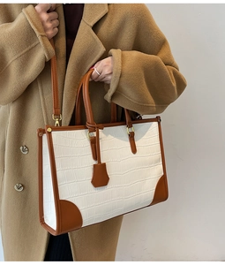 Detail of white crocodile texture tote bag with brown handles held by a model in a coat