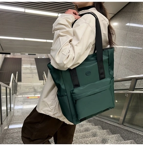 Detail view of dark green nylon tote bag featuring front zip pocket and sturdy straps