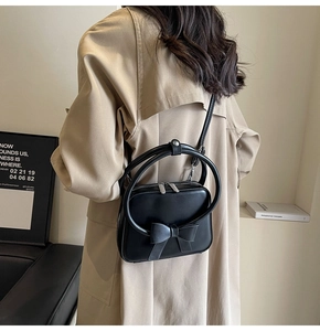 Detailed side view of a black bow leather crossbody bag worn with a beige trench coat