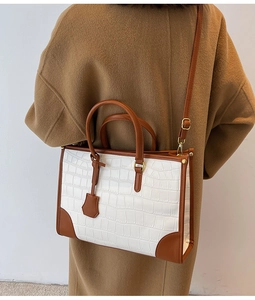 Detail of white crocodile pattern tote bag with brown leather straps and gold metal accents