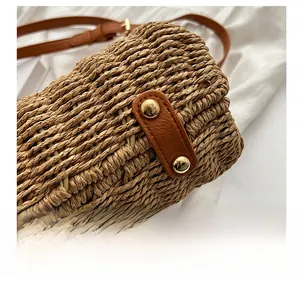 Close-up of hand-woven straw bag with brown leather base and golden protective rivets