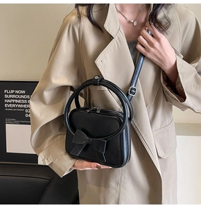 Detail of black glossy crossbody bag with round handle and bow on a trench coat model
