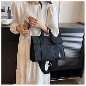 Detail of black canvas messenger bag featuring a flap closure and adjustable wide strap