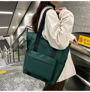 Macro detail of large nylon tote bag in dark green featuring front zip pocket and side pouches