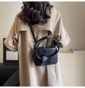 Detail of elegant black leather handbag with 3D bow decoration and round double handles