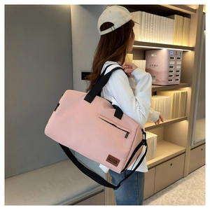 Close-up of pink Oxford cloth travel bag showing wide black straps and brown leather logo