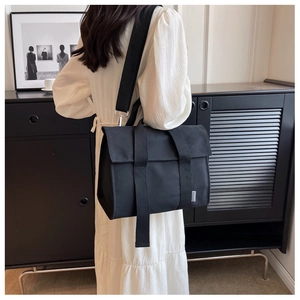 Detail of black canvas messenger bag with wide straps and silver metal hardware accents