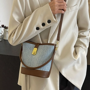Blue denim and brown leather bucket bag with gold lock shown on model's shoulder