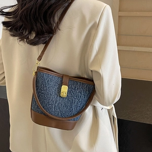 Chic blue denim bucket bag with brown leather trim and gold oval lock shown on model