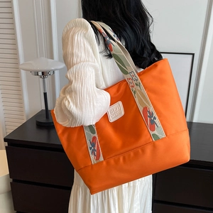 Orange nylon tote bag with floral embroidery strap and logo patch for daily commuting