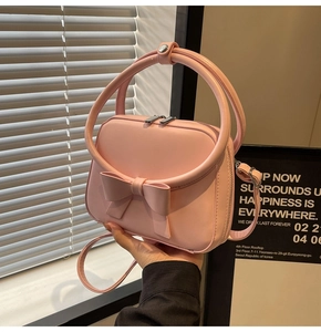Detail of a pink handbag with large bow decoration and round handles being held by a model