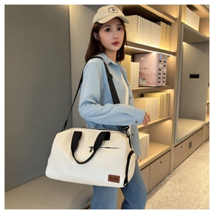 Detailed side view of an ivory canvas travel bag with black straps on a female model