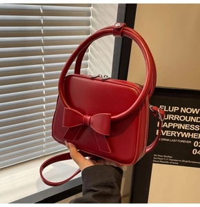 Detail of red crossbody bag with 3D bow decoration and unique round metal handle