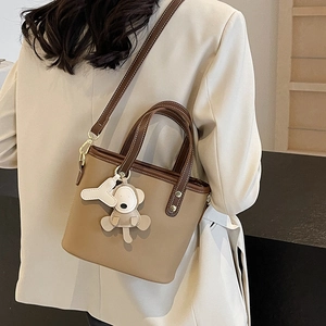 Brown bucket bag with contrast stitching and bear charm shown on a female model