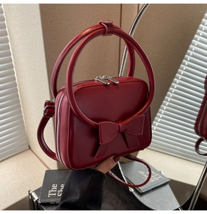 Detail of burgundy PU leather bag showing large round handle and elegant bow ornament