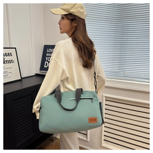 Detail of mint green Oxford cloth travel bag showing zipper pocket and black shoulder straps