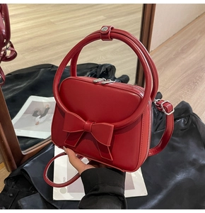 Detail of red synthetic leather handbag featuring a stylish 3D bow and round handles