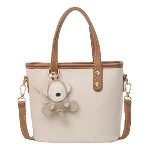 Beige bucket bag with brown trim and cute monkey charm, shown in front view with strap