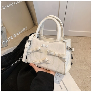 Detail der cremeweißen Faltenhandtasche mit dekorativen Schleifen und Perlenakzenten