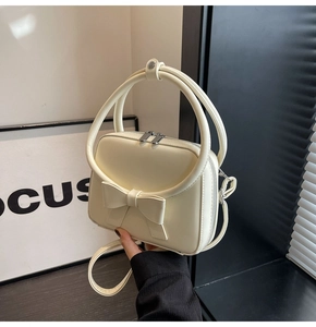 Detailed view of the creamy white crossbody bag with a 3D bow and silver zippers