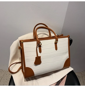 Detail of white crocodile texture tote bag with brown leather handles and gold hardware