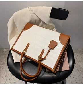 Detail of white crocodile pattern tote bag with brown handles and golden hardware accents