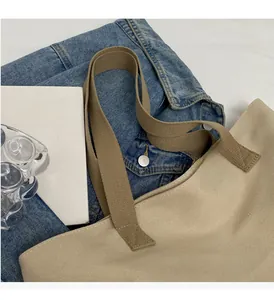 Detail of beige canvas tote bag with brown straps styled on a blue denim jacket