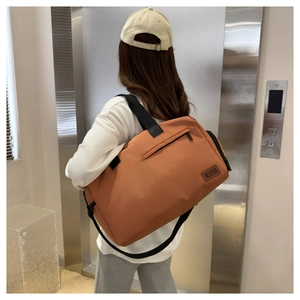 Close-up of large orange Oxford travel bag being carried by model in a modern elevator