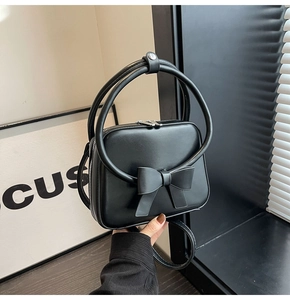 Detail of black handbag with large bow, circular handles, and smooth leather texture