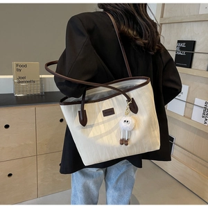 Detail of cream tote bag with leaf texture, plush charm and adjustable brown strap