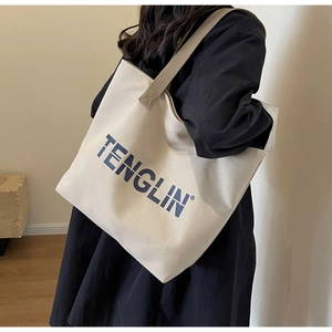 Detail of a large off-white canvas tote bag with blue branding carried by a model