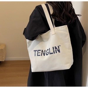 Detail of white canvas tote bag with blue text logo styled with a black coat