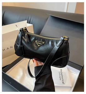 Detail of black pleated leather underarm bag with golden triangular logo and premium finish