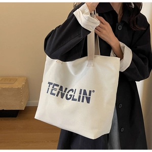 Side view of white canvas tote bag with blue lettering and beige fabric shoulder straps