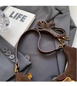 Detail of dark brown suede crossbody bag with gold J-shaped hardware on grey blazer