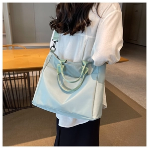 Rear view of a model wearing a light green nylon tote bag with adjustable shoulder strap