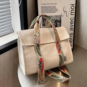 White canvas tote bag with colorful floral embroidery on the wide shoulder strap