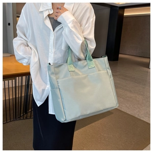 Close-up of mint green nylon tote bag featuring front open pocket and thick shoulder straps